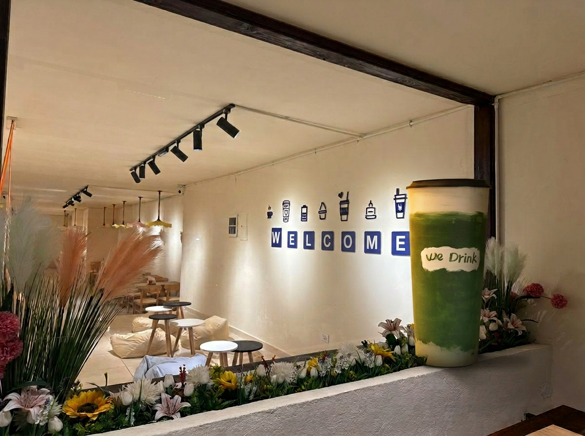 WeDrink café interior with the signature large matcha cup, warm lighting, bean bags, and flowers